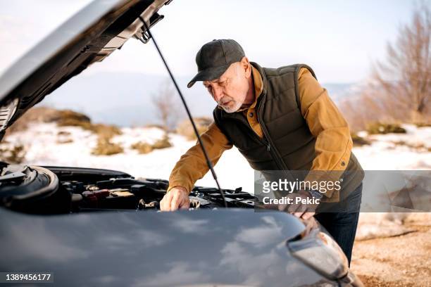 älterer mann mit seinem kaputten auto am rande einer landstraße - winter panne auto stock-fotos und bilder