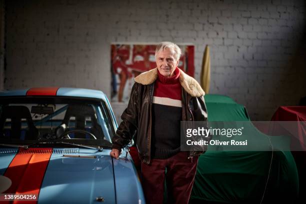 portrait of confident senior man with vintage sports car in garage - sportwagen stock-fotos und bilder