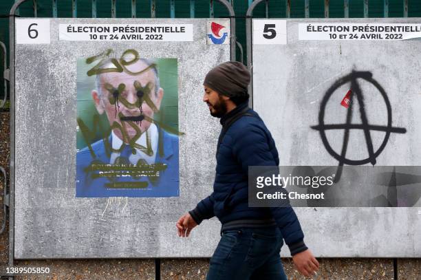 Man walks past a tagged official campaign poster of Far-right party "Reconquete!" leader, media pundit Eric Zemmour and another tagged with the...