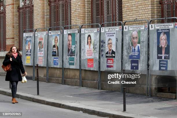 Woman walks past official campaign posters of the candidates for the 2022 presidential election displayed on billboards next to a polling station on...