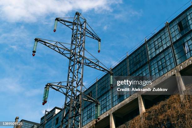 working towers of a high-voltage power line against a blue sky with clouds. the power supply line is overgrown with greenery and climbing grass. nearby is a building in dry grass. - georgia steel stock pictures, royalty-free photos & images