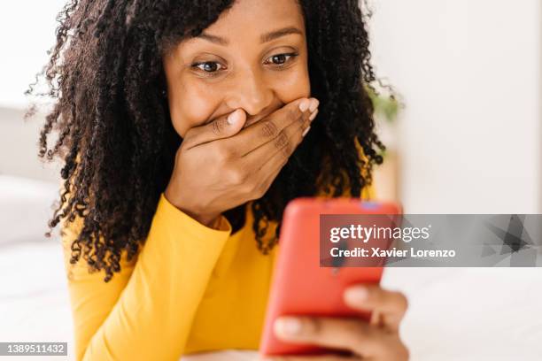 african american woman with a shocked expression on her face while looking at her mobile phone. - shock stock pictures, royalty-free photos & images