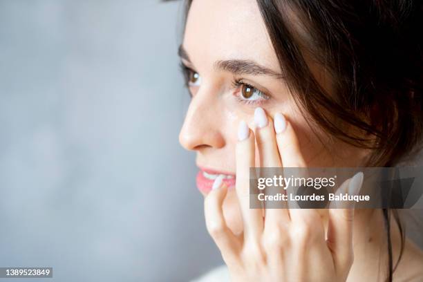 woman applying eye cream - antiarrugas fotografías e imágenes de stock