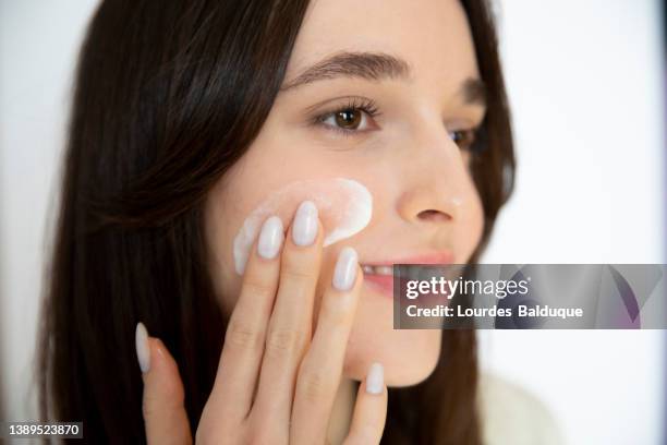 woman applying moisturizer to cheek - 乳液 ストックフォトと画像