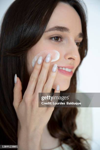 woman applying moisturizer to cheek - beautiful women spreading stock-fotos und bilder