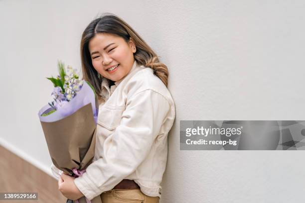 花を手にカメラを見つめる美しい女性のクローズアップポートレート - buxom women ストックフォトと画像