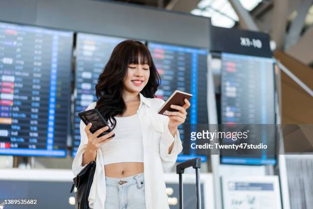 asian young woman standing in front of the flight schedule in the airport departure hall - business woman schild stock-fotos und bilder