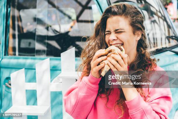smiling woman eating hamburger. - breaded fotografías e imágenes de stock