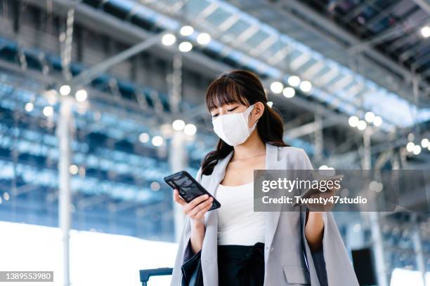 asian young businesswoman wearing a face mask using phone standing in the airport terminal - airport mask stock pictures, royalty-free photos & images