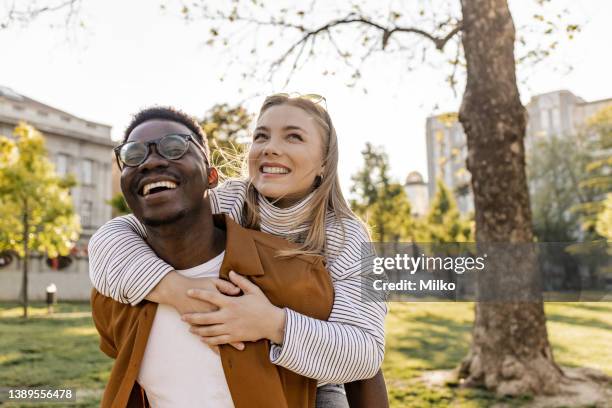 interracial couple piggybacking outdoors - park couple piggyback stock pictures, royalty-free photos & images