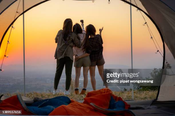 girl friend group asians laying in tents during camping are waking up to watch the sun rise and shoot video from their action cams to show off to their friends in social media - mid twenties fun foto e immagini stock