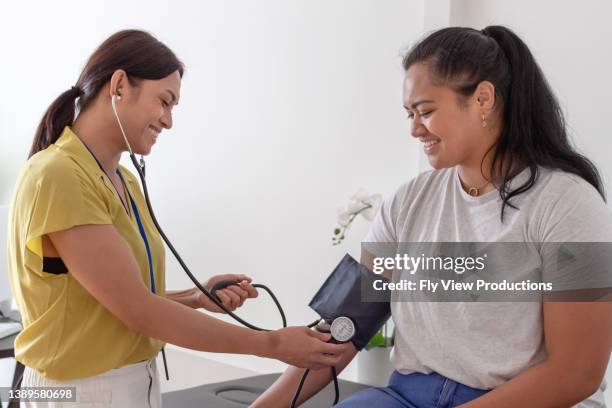 young pacific islander woman having blood pressure measured by doctor - pacific islander stock pictures, royalty-free photos & images