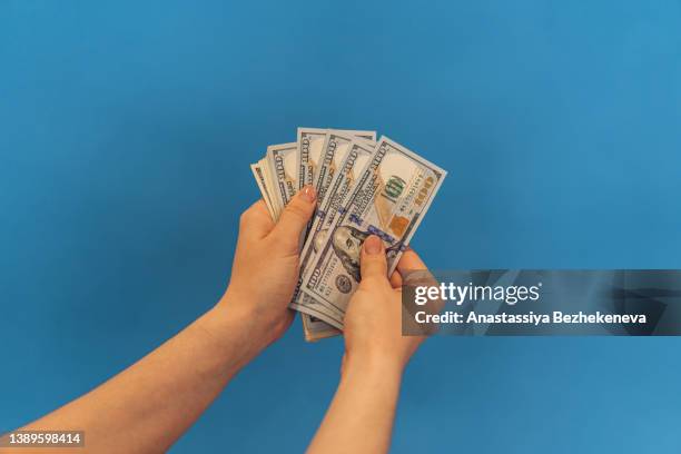 women's hands holding one hundred dollar bills in fan against blue background - 100 dollar bill new stock pictures, royalty-free photos & images