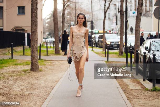 Model Ashley Radjarame attends the Ludovic de Saint Sernin show in a gold shimmer distressed slip dress, pink heels, black purse during Paris Fashion...