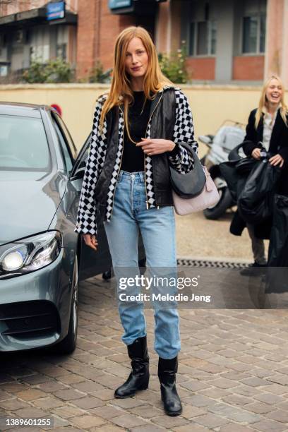 Dutch model Rianne van Rompaey wears a black and white checkered vest jacket, small Coperni bag, pink purse, mid-rise blue jeans tucked into black...