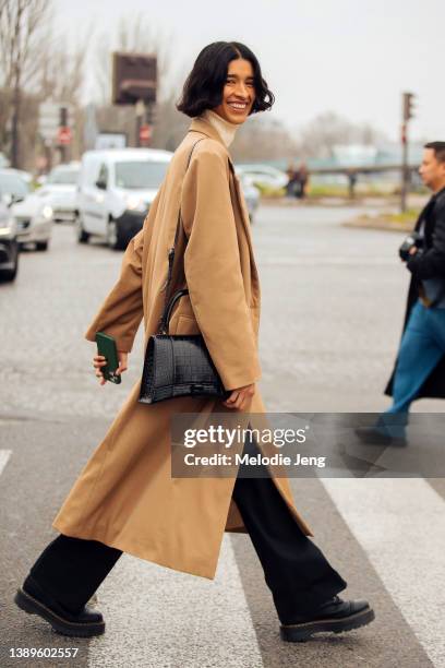 Mexican model Marsella Rea wears a long tan coat, black leather Balenciaga bag, black pants, black boots after the Loewe show at Tennis Club de Paris...