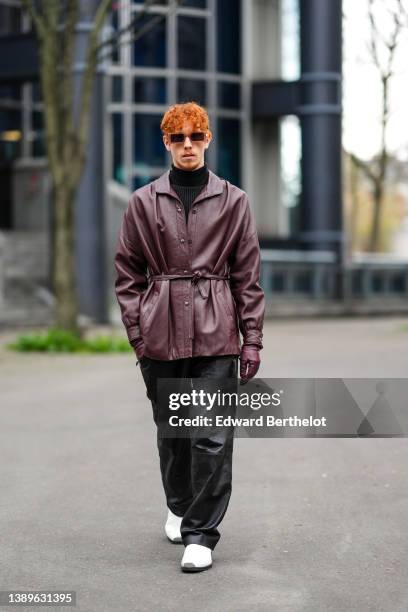 Guest wears brown square sunglasses, a black ribbed wool turtleneck pullover, a burgundy shiny leather belted shirt jacket, black shiny leather large...