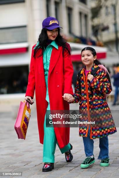 Guest wears purple with embroidered yellow pattern cap, a green mint leather belted jacket, green mint shiny leather large pants, a red long coat, a...