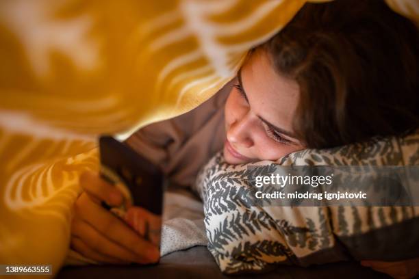 teenage girl, using her mobile phone under the bed sheet - girl in her bed stockfoto's en -beelden