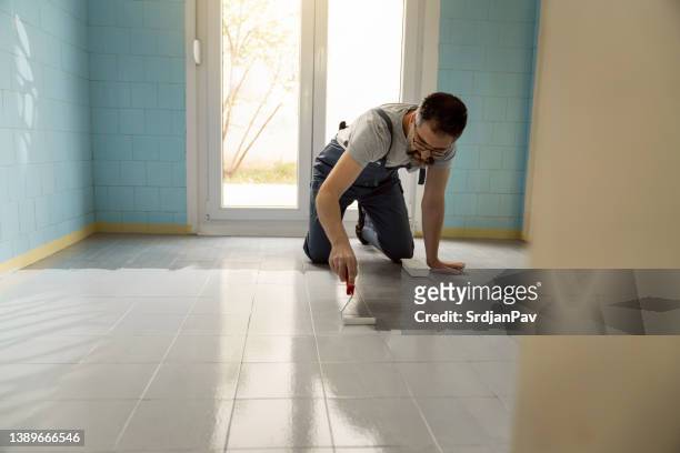 caucasian house painter, kneeling while painting the floor tiles in the kitchen - kitchen straighten stockfoto's en -beelden