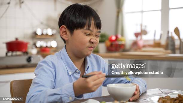 closeup of unhappy asian japanese little boy making a disgust expression while looking at green vegetable in bowl and shaking head show dislike and put it back at dining table - hate broccoli stock pictures, royalty-free photos & images