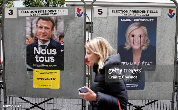 Woman walks past official campaign posters of Marine Le Pen, leader of the far-right Rassemblement national party and French President Emmanuel...