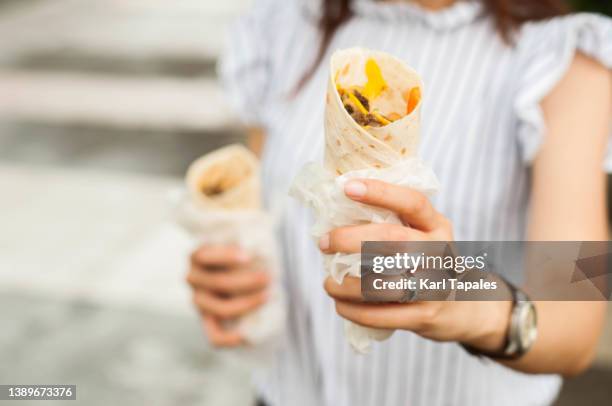a southeast asian woman is holding take-out wrap sandwich outdoors - greek food stock pictures, royalty-free photos & images