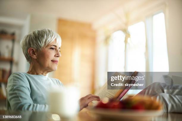 senior woman reading a book at home. - white book stock pictures, royalty-free photos & images