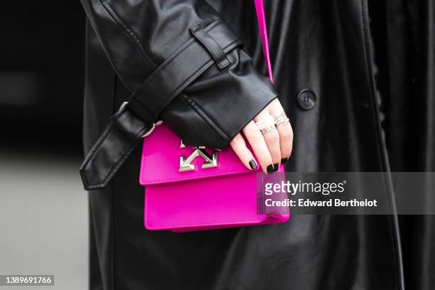 Guest wears a black shiny leather long coat, silver rings, a neon pink shiny leather shoulder bag from Off-White , outside Gauchere, during Paris...