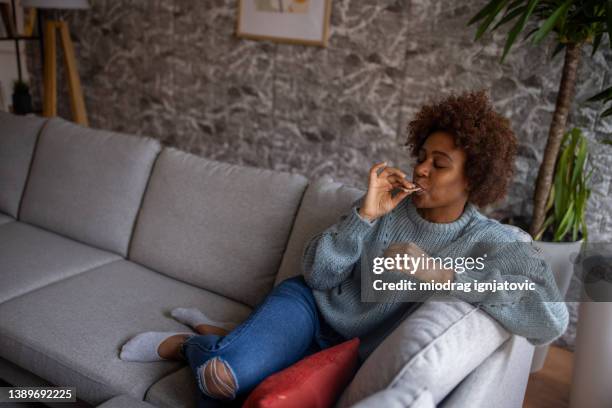 mujer joven etnia negra sentada en el sofá y comiendo chocolate - barra de chocolate fotografías e imágenes de stock