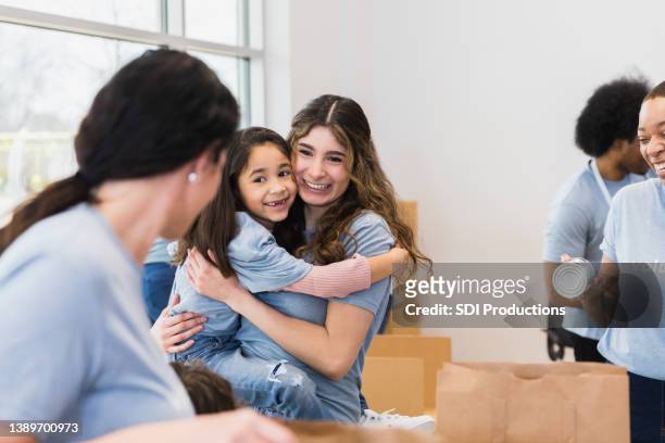 tía adulta joven abraza a sobrina de edad primaria en colecta de alimentos - niece fotografías e imágenes de stock