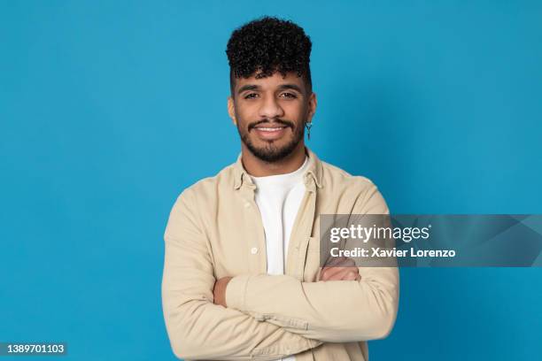 trendy young latino man llooking at the camera and smiling while posing with his arms crossed. - venezuelans stock pictures, royalty-free photos & images