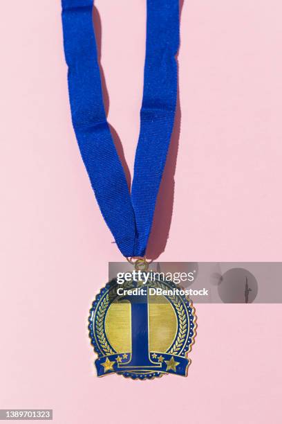 first place champion medal with number 1 in blue and blue strap on a pink background. concept of competition, winner, winner, sport, triumph, champion and first place. - praticando imagens e fotografias de stock