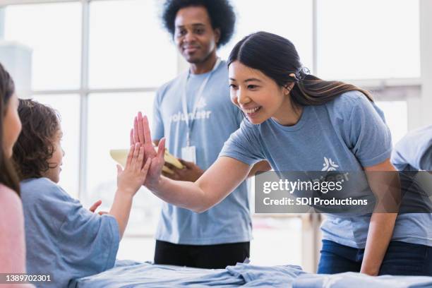 young adult woman high fives child volunteer - charity drive stock pictures, royalty-free photos & images
