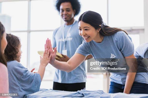 young adult woman high fives child volunteer - non profit organization stock pictures, royalty-free photos & images