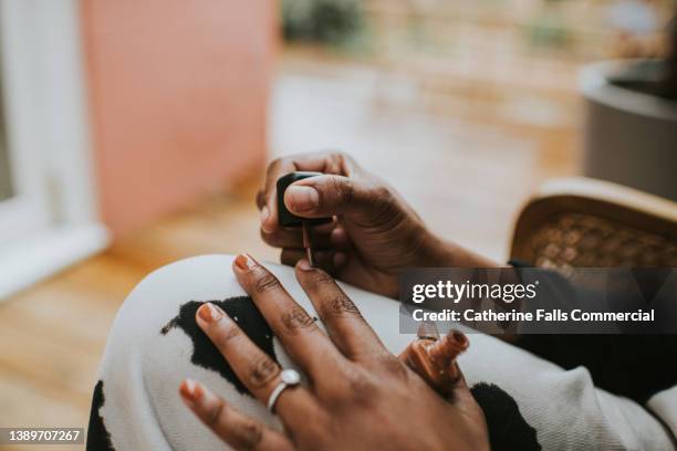 close-up of a black woman painting her fingernails brown - painting fingernails stock pictures, royalty-free photos & images