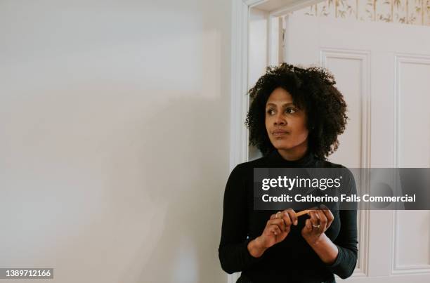 simple image of a beautiful young black woman standing in an interior doorway, filing her nails. - face expressions stock pictures, royalty-free photos & images