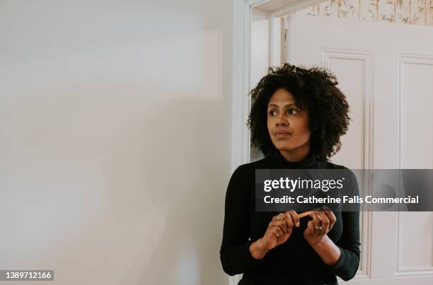 simple image of a beautiful young black woman standing in an interior doorway, filing her nails. - boring face expression stock pictures, royalty-free photos & images