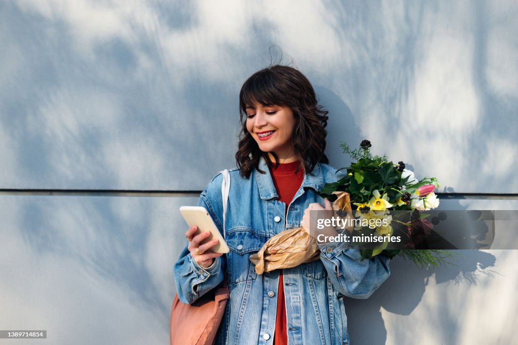 Beautiful Woman Leaning Against a Wall and Holding Flowers