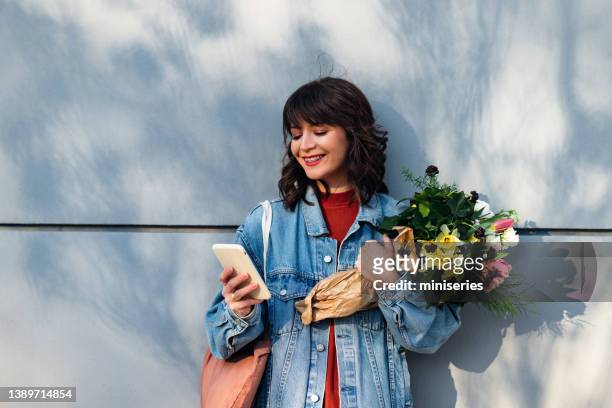 beautiful woman leaning against a wall and holding flowers - multi colored jacket stock pictures, royalty-free photos & images
