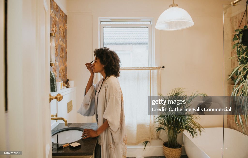 Beautiful black woman applies make-up in a bathroom mirror