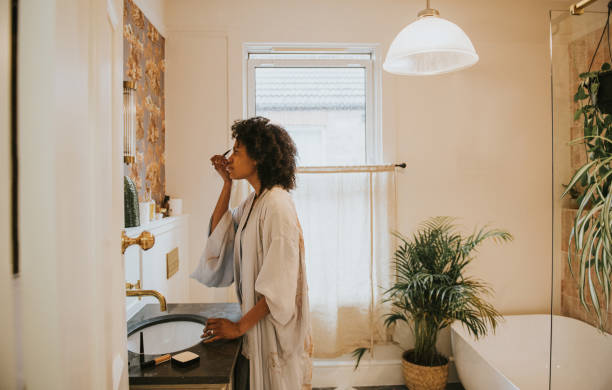 beautiful black woman applies make-up in a bathroom mirror - makeup stock pictures, royalty-free photos & images