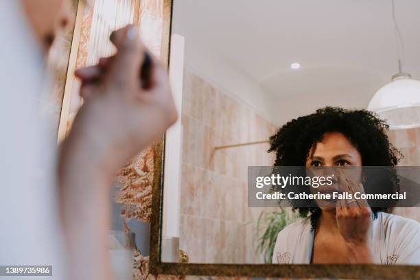 a beautiful woman applies concealer under her eyes - concealer foto e immagini stock