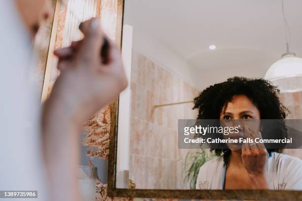 a beautiful woman applies concealer under her eyes - concealer stock pictures, royalty-free photos & images