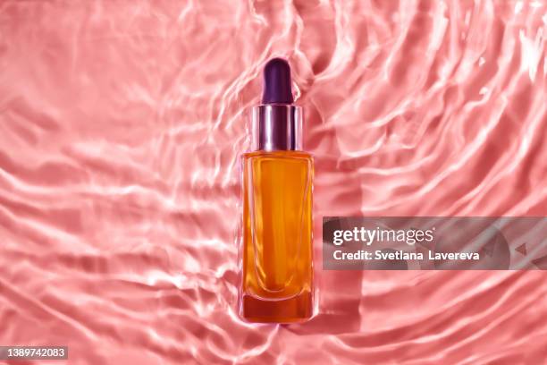 flatlay of bottle with serum lying down in pink rippling water. underwater effect. stylish concept of organic essences, sea health products. copy space, minimalism, flat lay. marine cosmetics - cosmetic bottle imagens e fotografias de stock