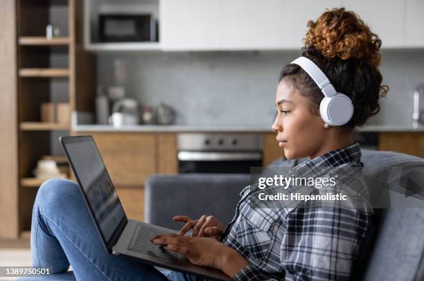 mujer en casa trabajando en su computadora portátil y usando auriculares - stream fotografías e imágenes de stock