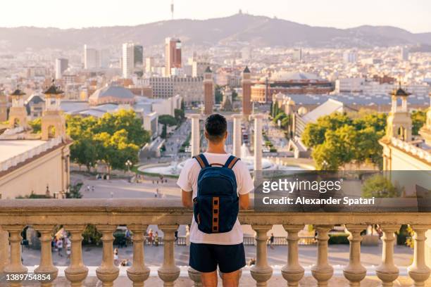 rear view of a young man with backpack looking at barcelona skyline from above, barcelona, spain - montjuic 個照片及圖片檔