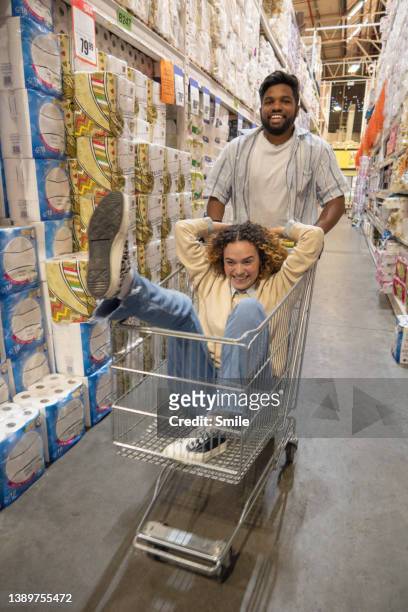 man pushing woman in a trolley down aisle - man pushing cart fun play stock pictures, royalty-free photos & images