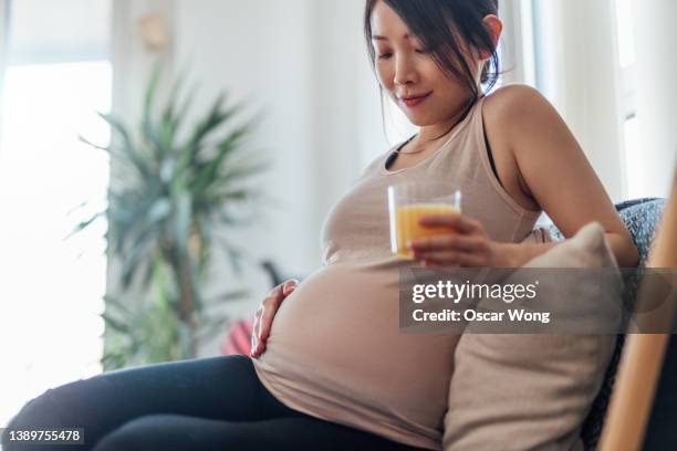 smiling pregnant woman drinking juice and relaxing at home - mom resting stock pictures, royalty-free photos & images