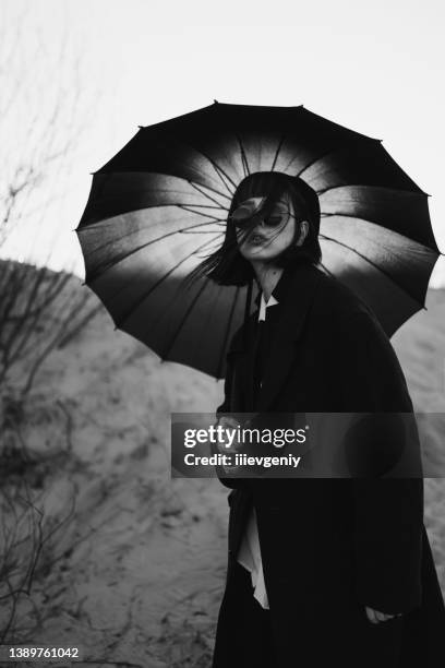 black white photography. redhead girl in black clothes outdoors. gothic style. asian fashion model in dark coat with umbrella on nature. bw photo. stylish outfit. subculture. monochrome. desaturated - asian goth girl stock pictures, royalty-free photos & images